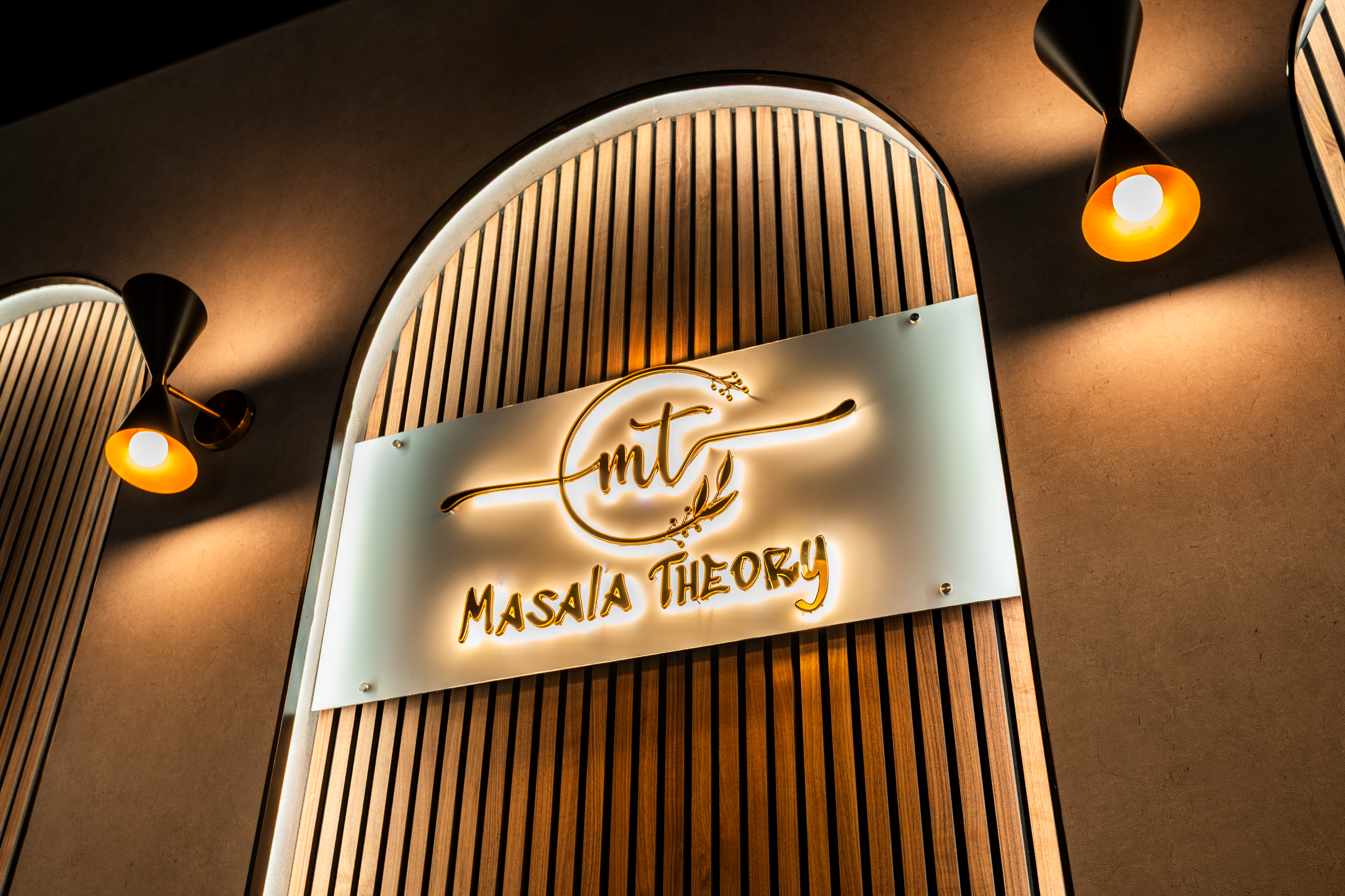 Illuminated Masala Theory sign on the wooden arch wall inside the Calgary SE bistro